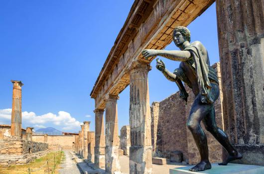 Statua antica e rovine a Pompei sotto un cielo azzurro.